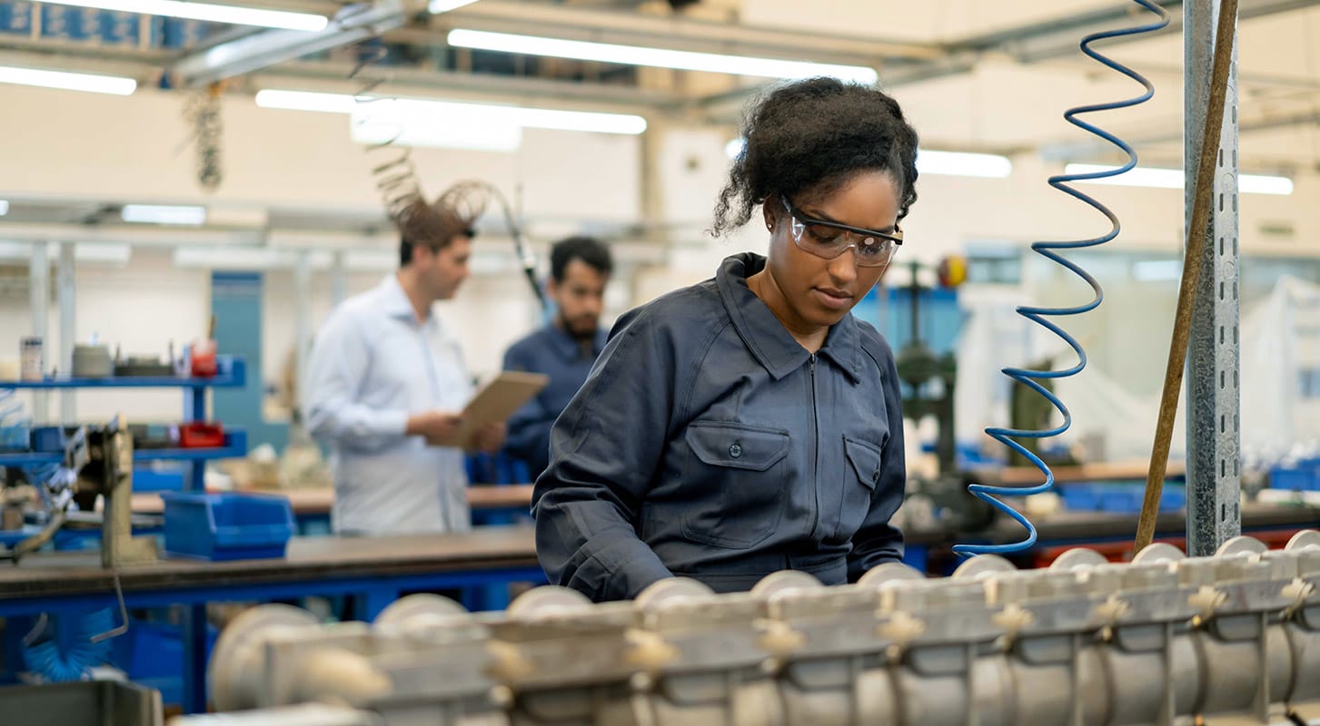 A woman operates machinery in a factory, focused on her work amidst industrial equipment and tools.